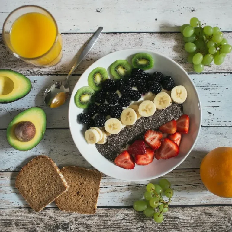 Bol de chia avec bananes, fraises, kiwis, baies, et tranches d'avocat, accompagné de jus d'orange.