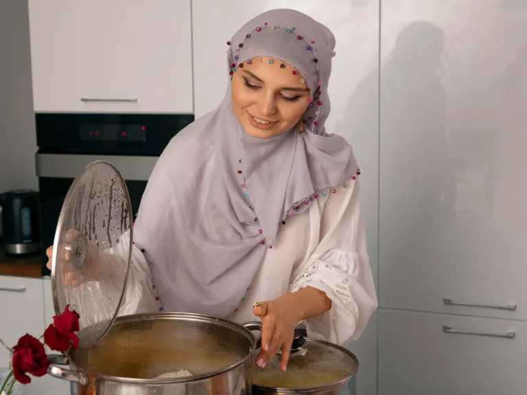 Femme en hijab souriante, remuant une grande casserole dans une cuisine moderne.