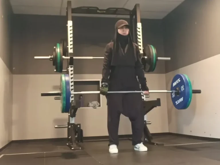 Muslima Fit soulève une barre avec des poids dans une salle de sport.