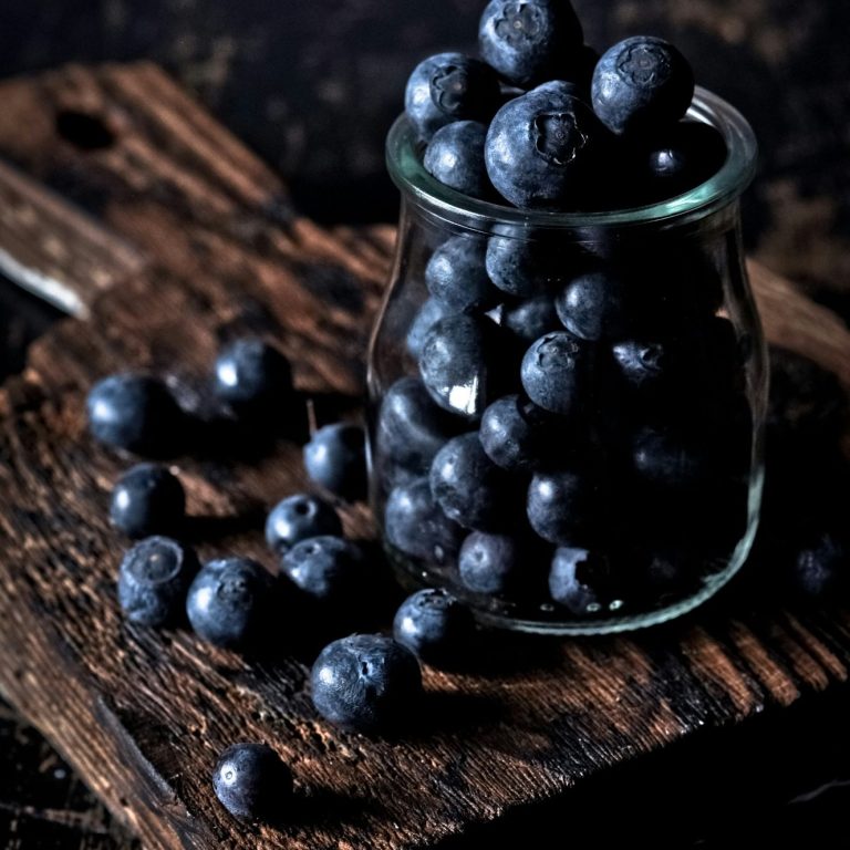 Des petits fruits bleus dans un pot en verre sur un fond en bois sombre.