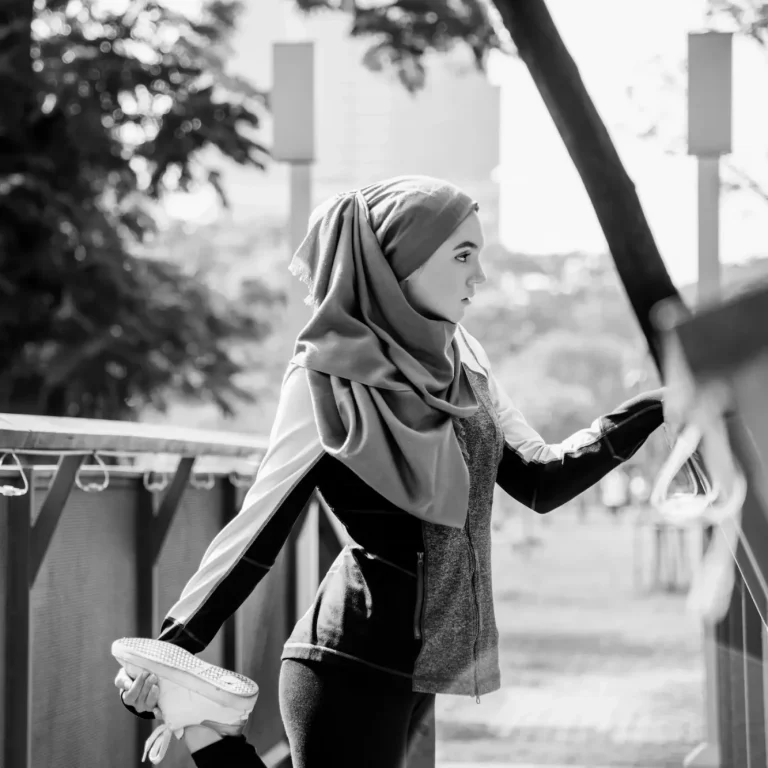 Femme en hijab faisant de l'exercice, tenant des chaussures de sport, en milieu urbain.