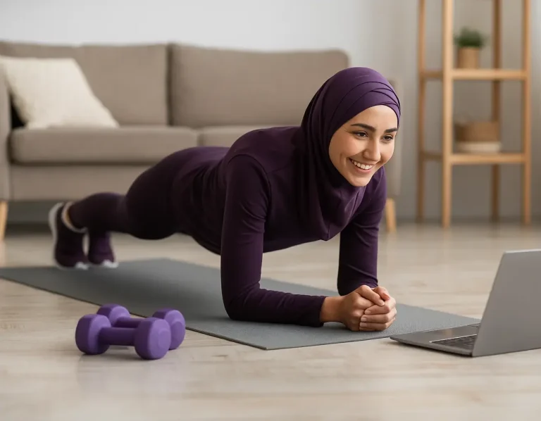 Femme en hijab faisant du fitness avec des haltères près d'un ordinateur portable.