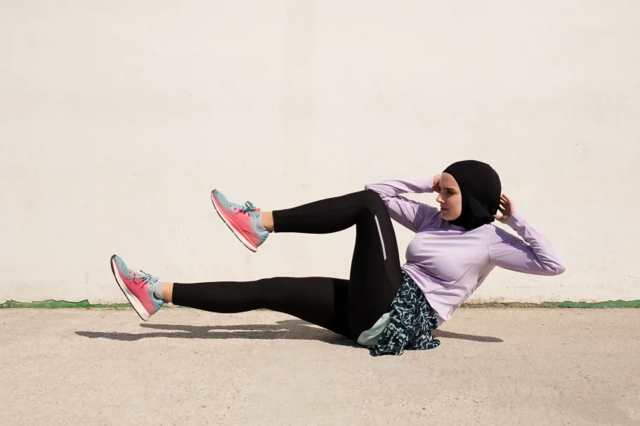 Femme en hijab s'exerçant au sol, faisant des abdominaux, vêtue de vêtements de sport.