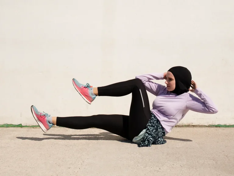 Femme en hijab effectuant un exercice de fitness au sol, vêtue de vêtements de sport.