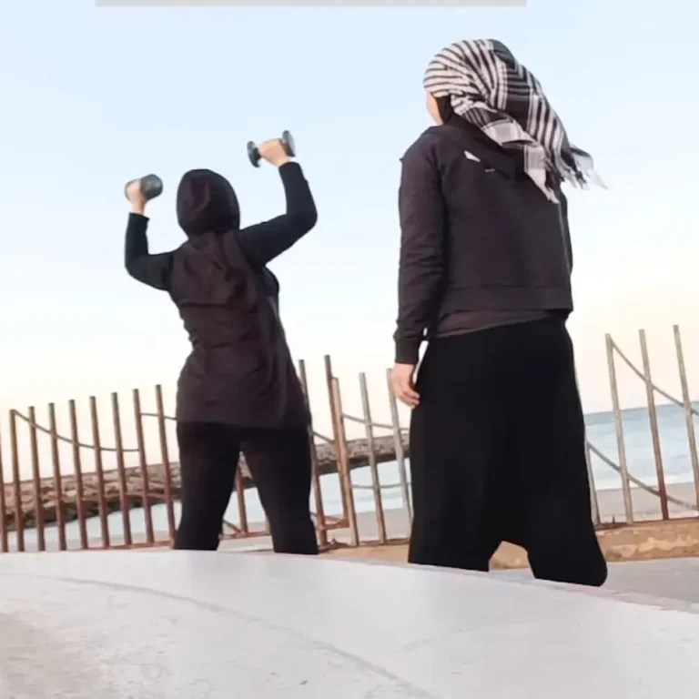 Coach Muslima Fit et son élève s'entraînent en levant des poids face à l'océan.