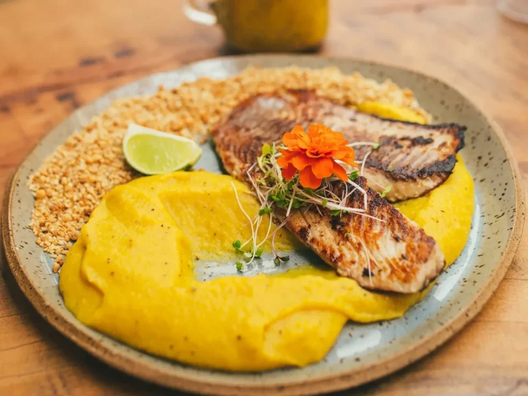Plat de poisson grillé avec purée jaune, riz, cirtron et fleur comestible.