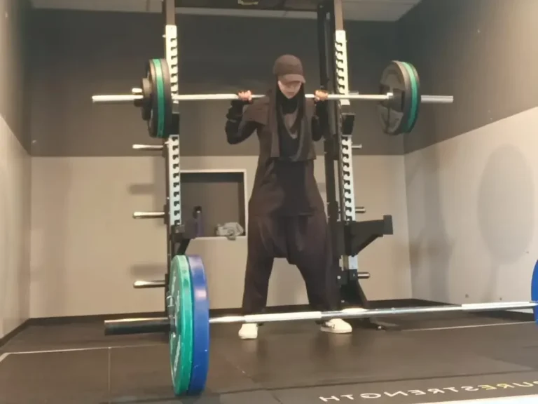 Femme en tenue de sport soulevant une barre avec des poids dans une salle de gym.