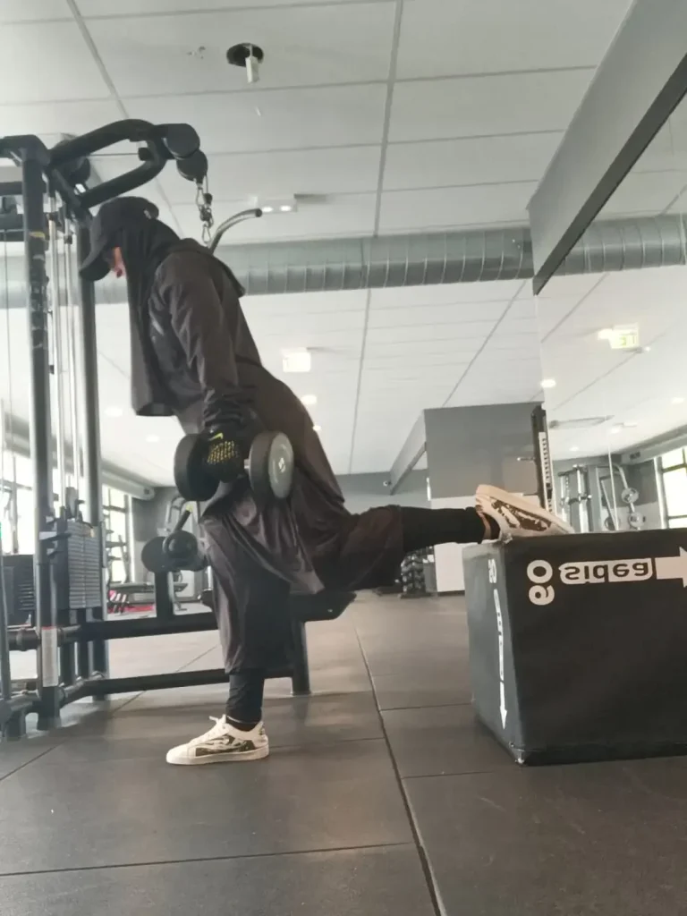 Coach Muslima Fit effectuant un exercice de musculation sur un appareil en salle de sport.